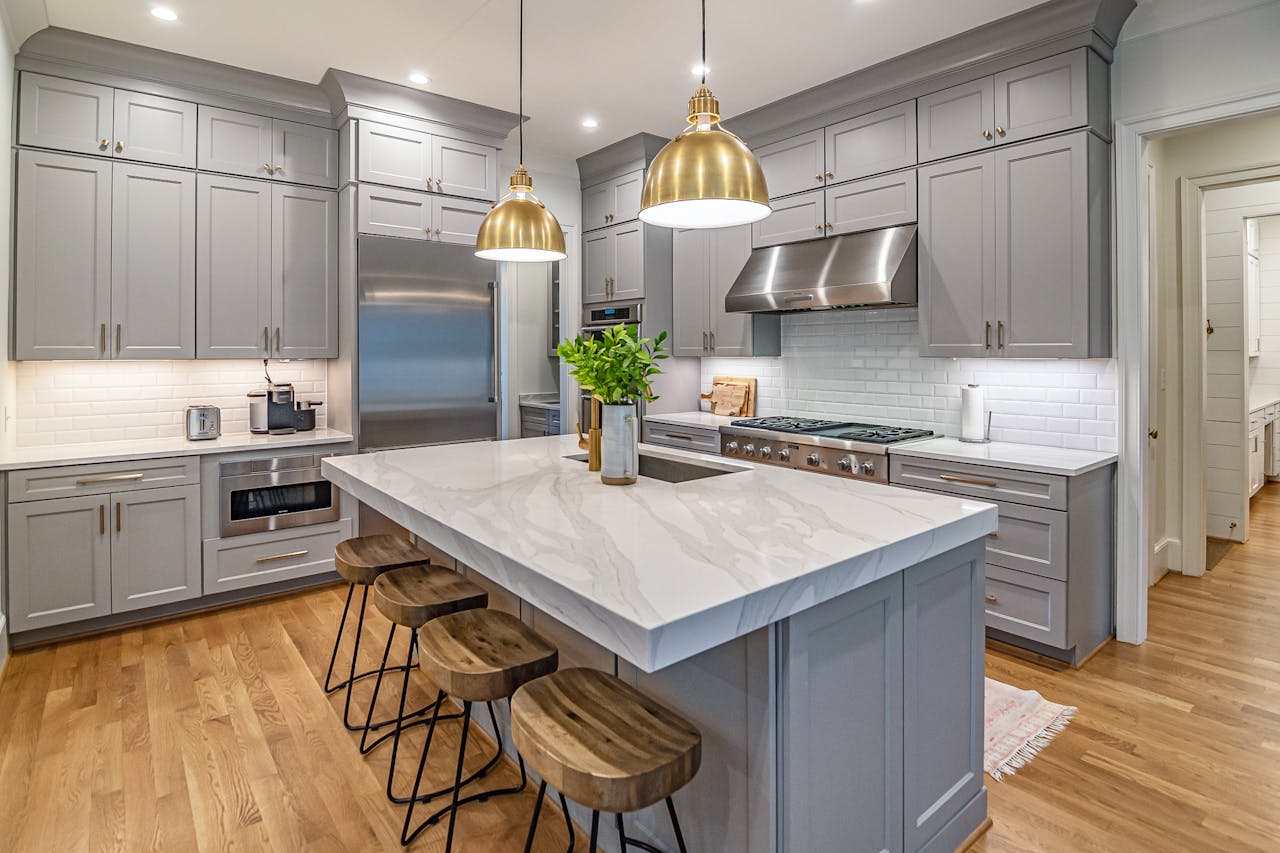 Stylish modern kitchen featuring a large marble island, gold pendant lights, and gray cabinetry.